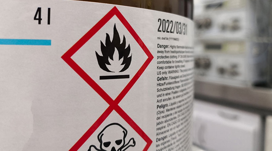 Chemical label close-up with flammability and toxicity hazard symbols, safety warnings, and expiration date clearly visible.