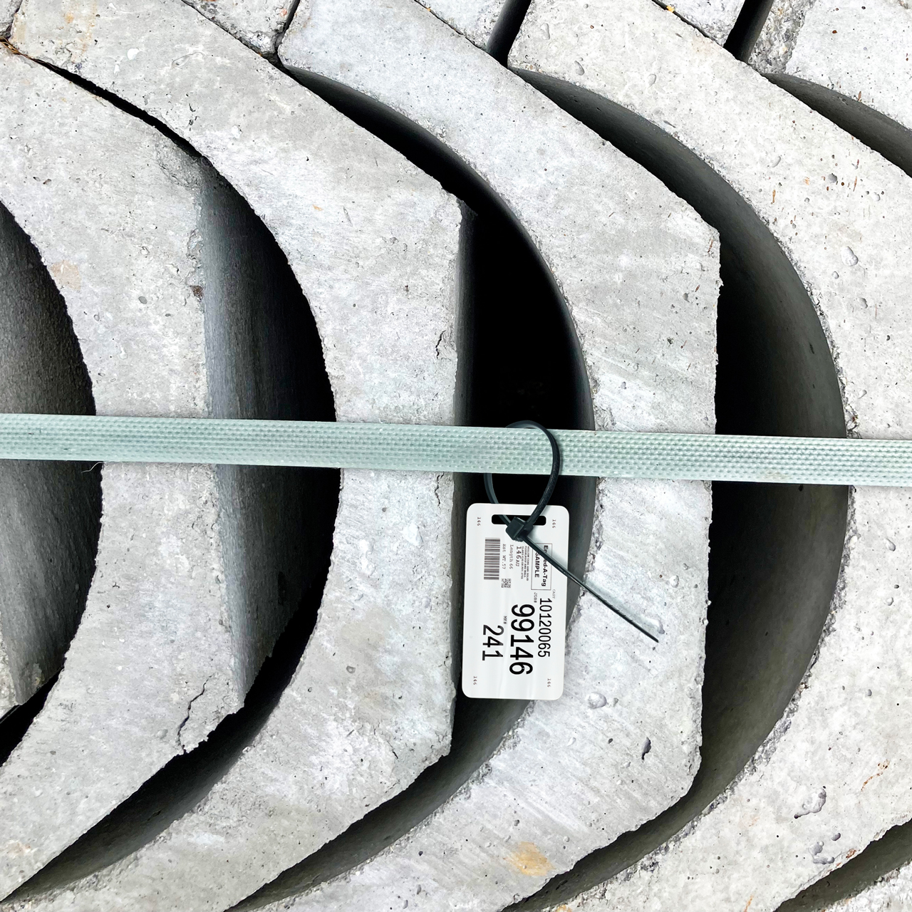 Stacked curved concrete slabs held by a green strap with a barcode tag attached at the center.