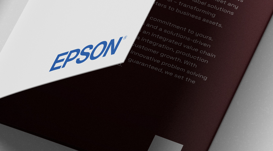 Booklet with white cover and blue EPSON logo overlays a maroon page with partially visible white text, shown in close-up view.