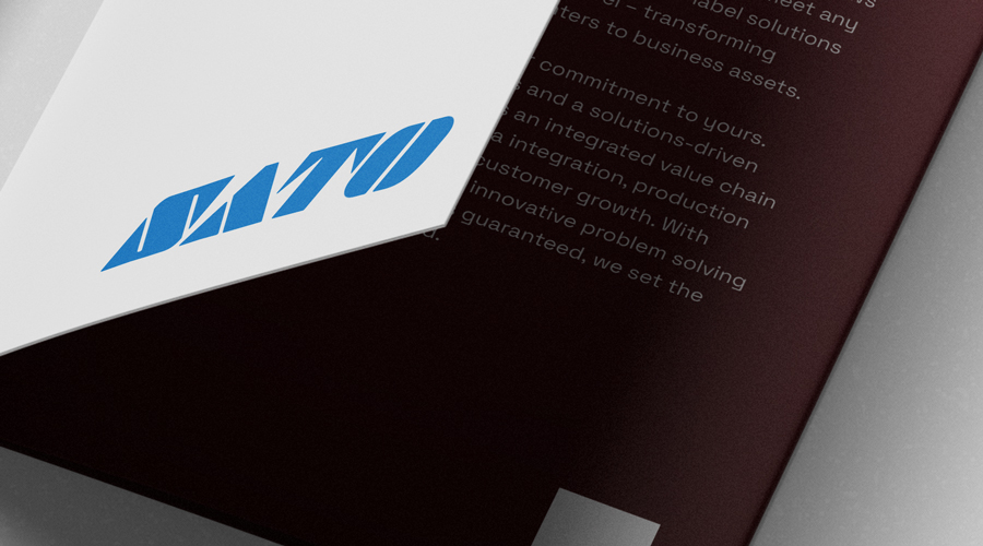 Open brochure close-up with white cover and bold blue geometric logo, maroon inside page with faint white text on a pale surface.