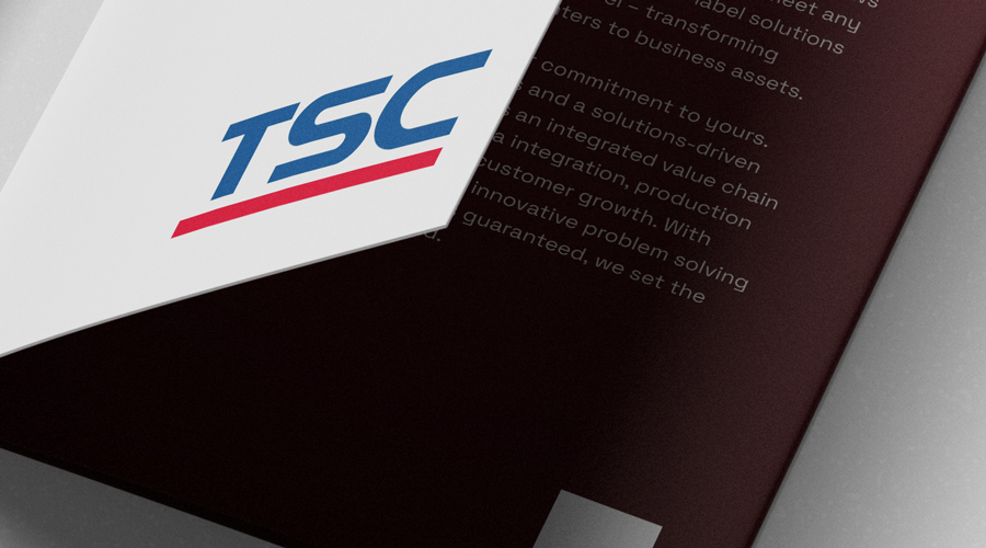 Close-up of folder with blue and red TSC logo, partially covering maroon page with white text in a professional business setting.