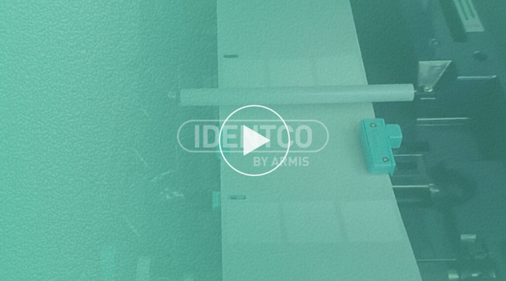 Teal-tinted close-up of a paper processing machine with a play button and center text: IDENTOO BY ABMIS.