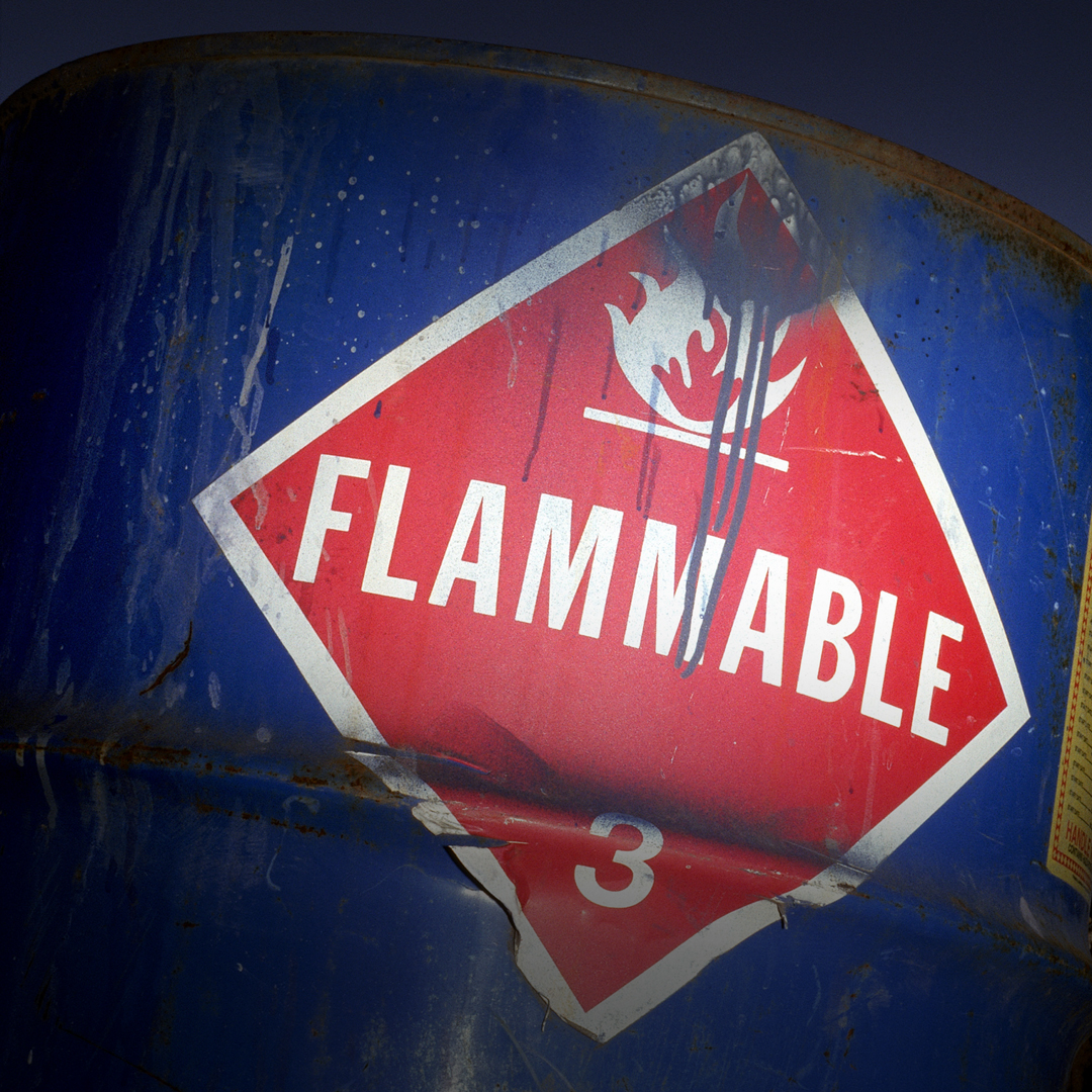 Close-up of blue metal barrel with worn, peeling red diamond flammable label, flame symbol, and number 3 at the bottom.