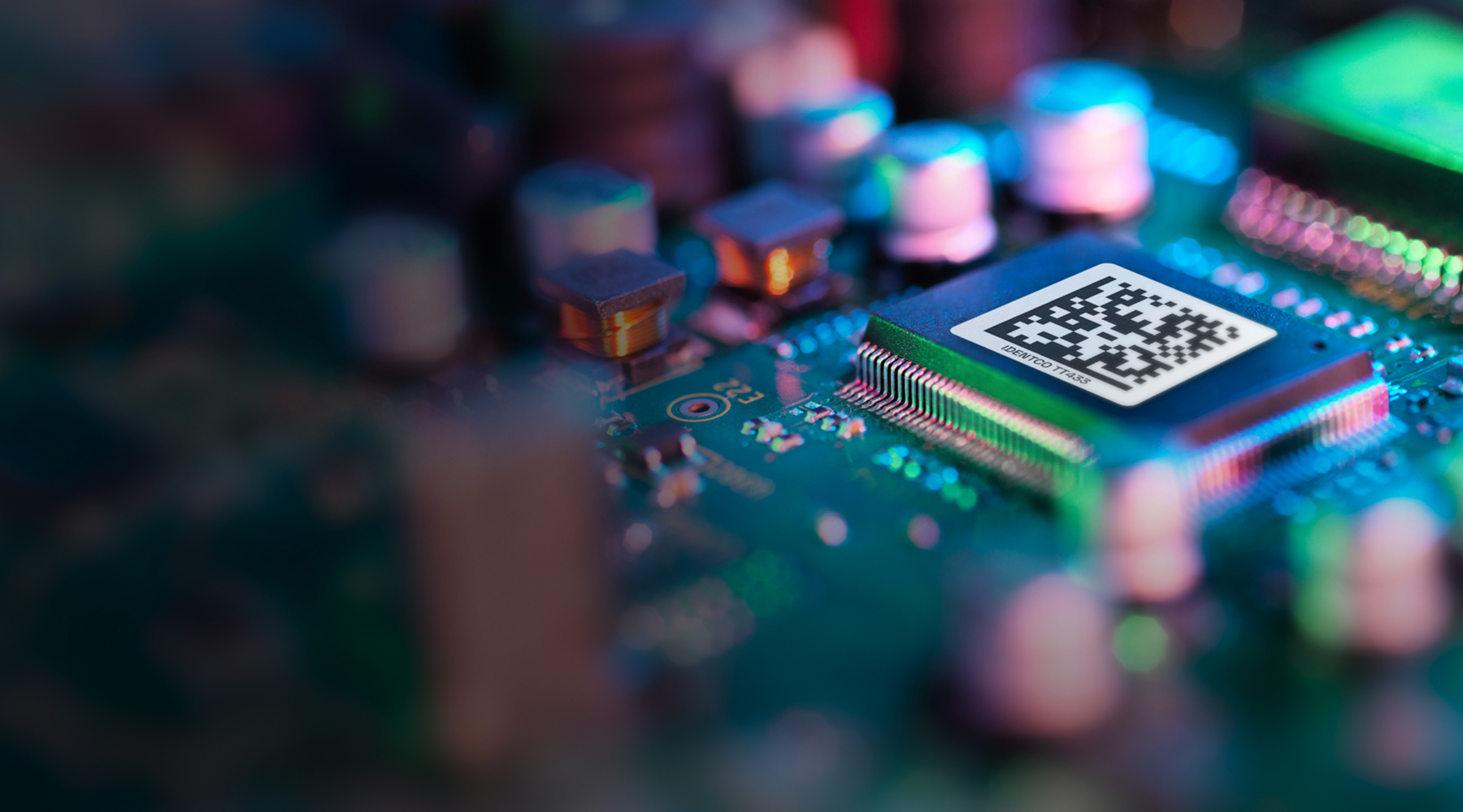 Microchip with QR code on a computer circuit board, surrounded by electronic components and colorful blurred lights.