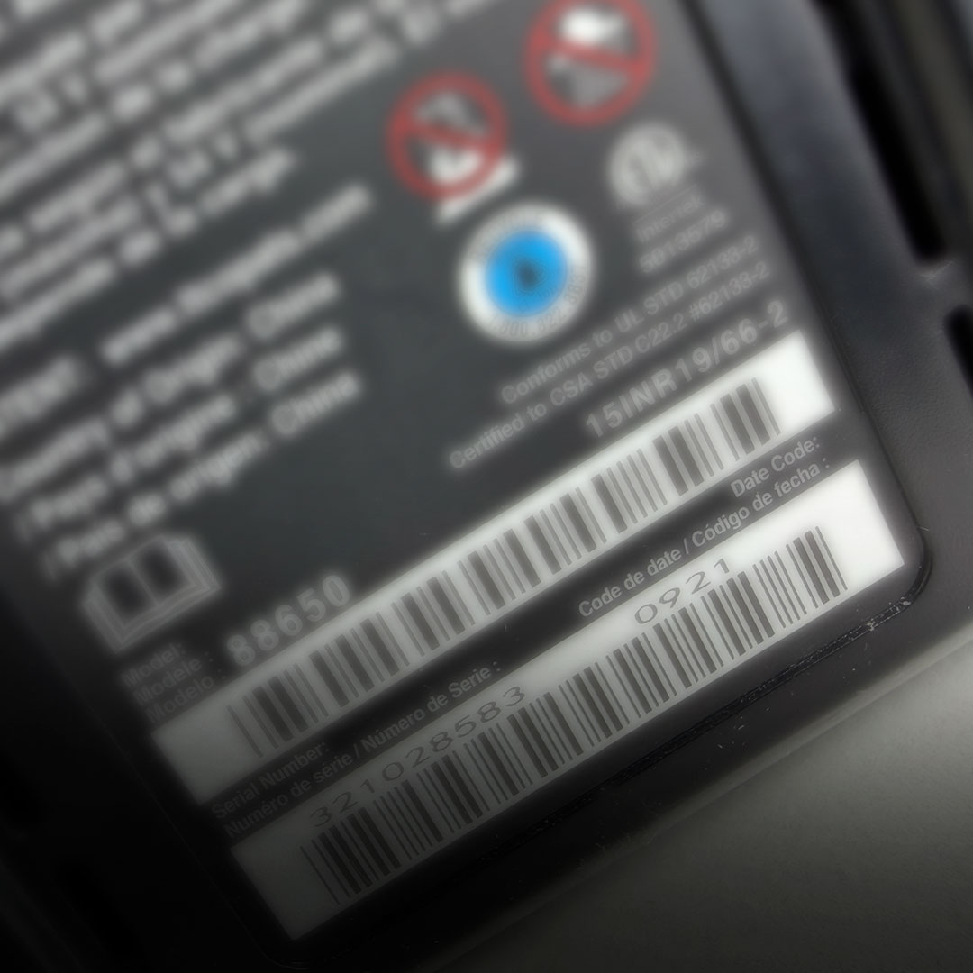 Close-up of product label with barcodes, numbers, safety icons, serial number, and date code in English and Spanish; slightly blurred.