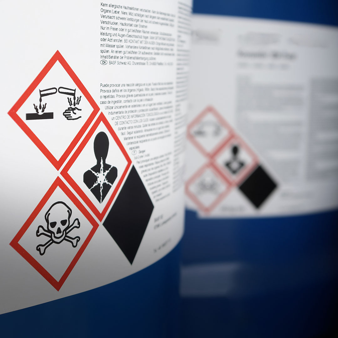 Chemical label close-up with corrosive, toxic, health hazard, and environmental danger symbols plus visible safety instructions.