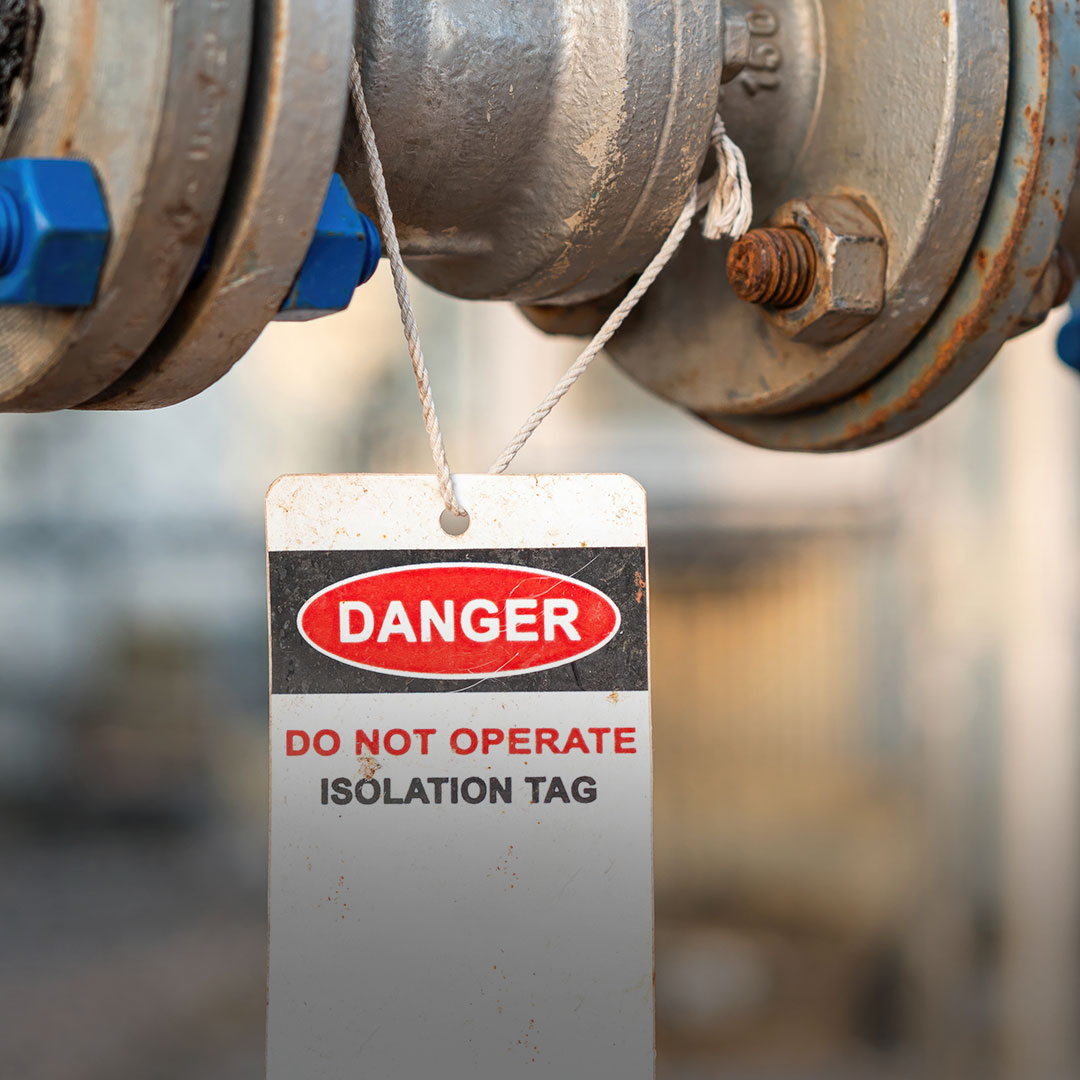 Close-up of a metal pipe with a bold warning tag stating danger, do not operate, isolation tag; blurred background.
