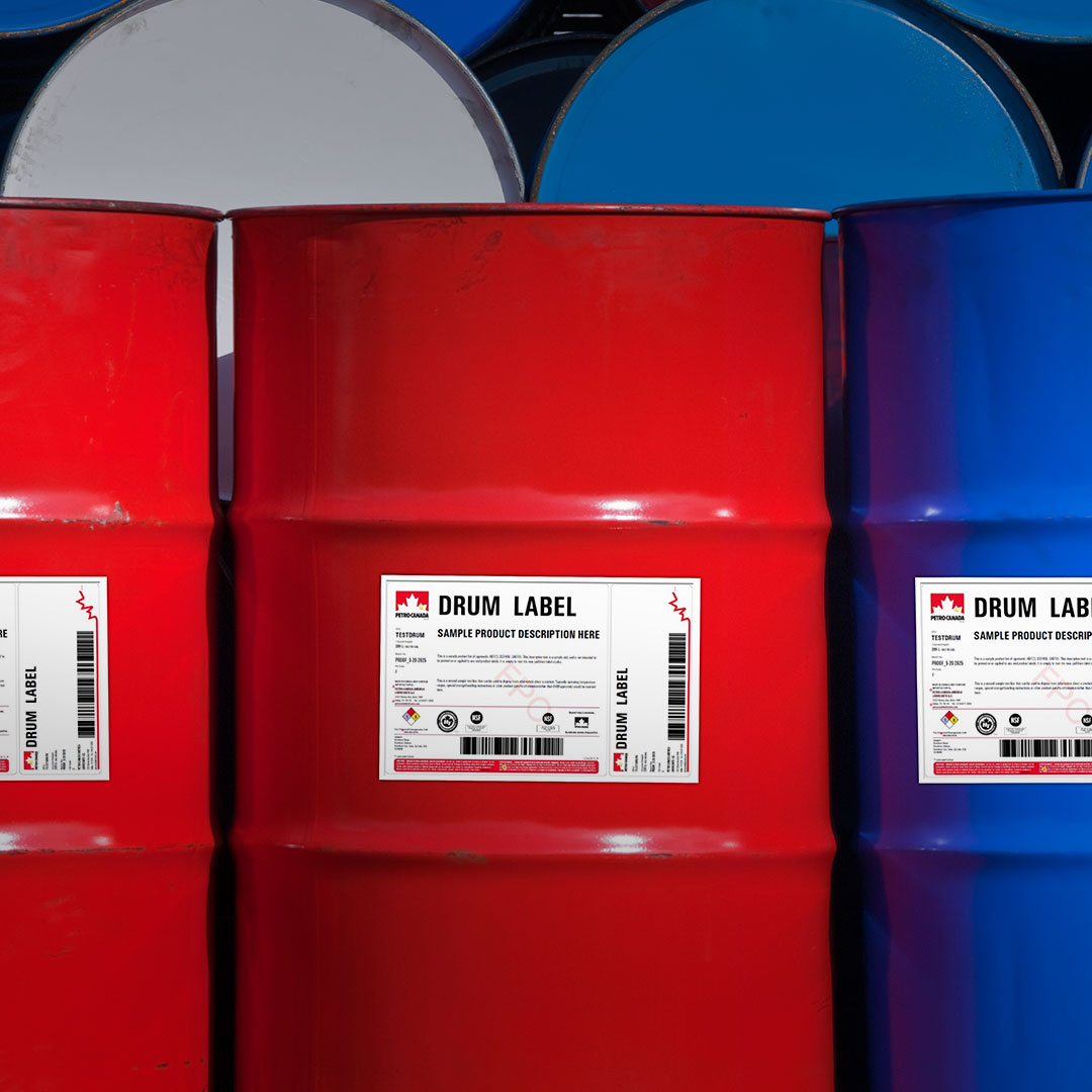 Three large metal drums, two red and one blue, labeled with white barcodes in an industrial warehouse with stacked blue drums.