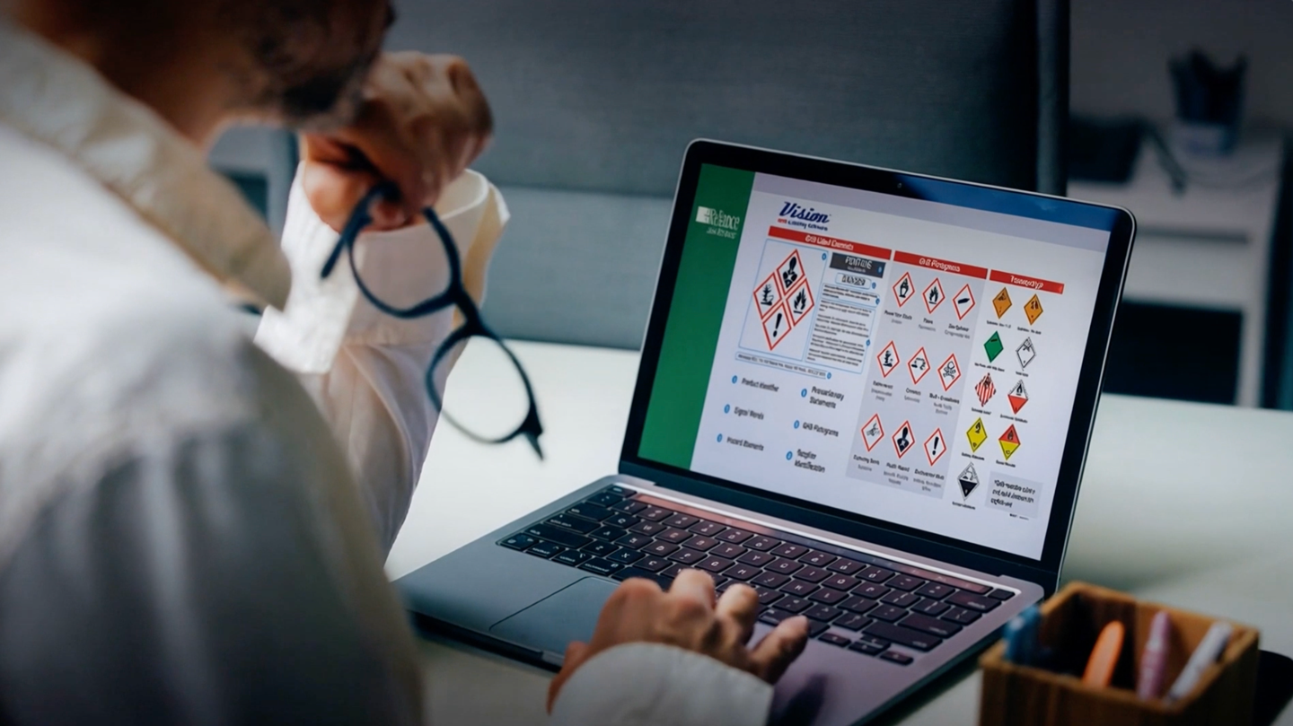 Person with glasses examines laptop screen showing hazardous material symbols and safety info, engaged in chemical safety training.